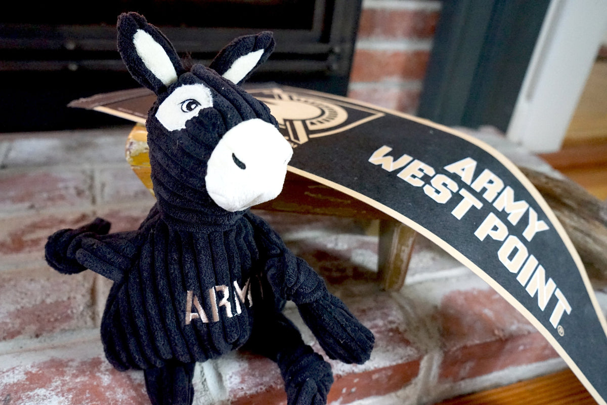 Army Mule Knottie dog toy on a brick hearth beside an Army West Point pennant