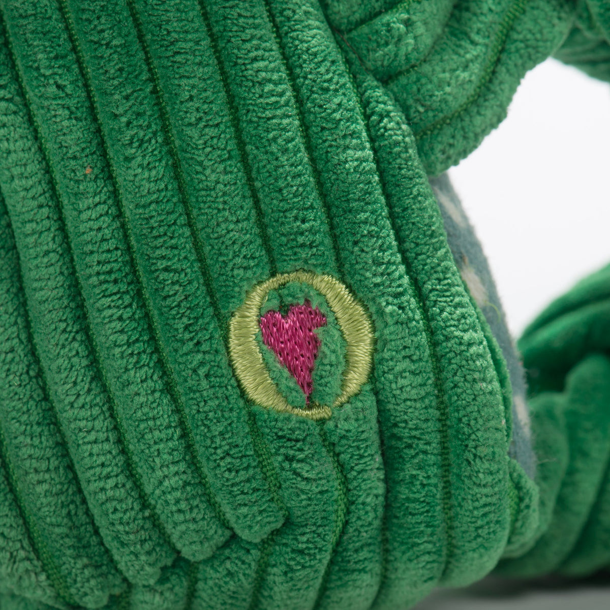 Fergie Frog Knottie close-up of the embroidered pink heart logo on its green corduroy