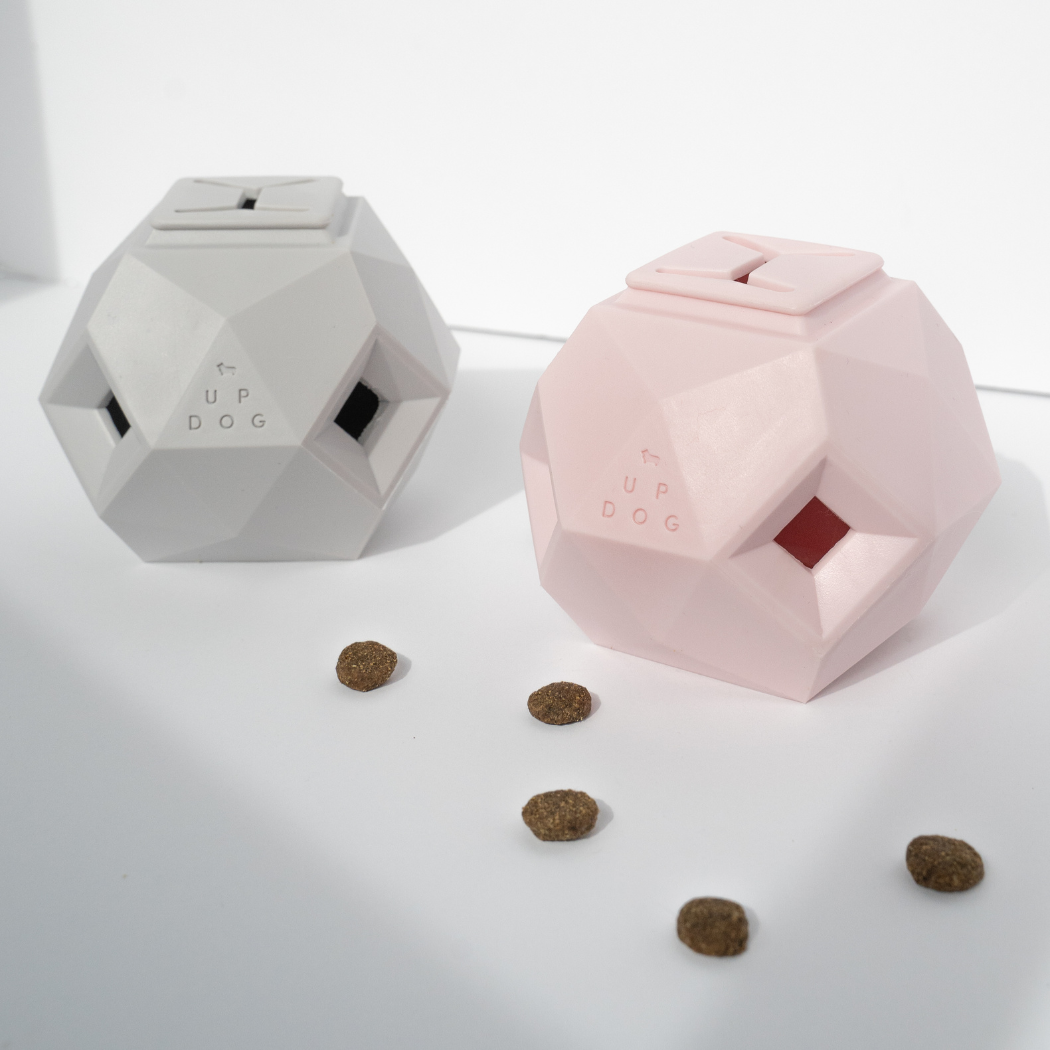Up Dog Odin Treat Puzzle Balls in light grey and rose quartz, two faceted treat toys with kibble scattered in front