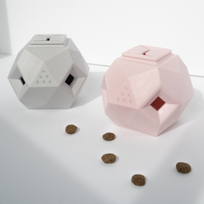 Up Dog Odin Treat Puzzle Balls in light grey and rose quartz, two faceted treat toys with kibble scattered in front