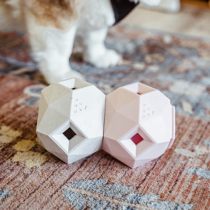 Up Dog Odin Treat Puzzle Balls in light grey and rose quartz, two linked side by side on a patterned rug