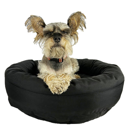 Round Bolstered Armor dog bed in black with a scruffy terrier mix resting in it, eyes closed, paws over the rim