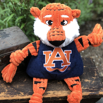 Aubie the Tiger Knottie dog toy sitting on a weathered wooden bench outdoors, one arm raised