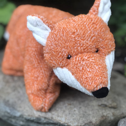 Squooshie Fox plush toy on a garden stone outdoors, close-up of its tweedy orange face and white corduroy ears