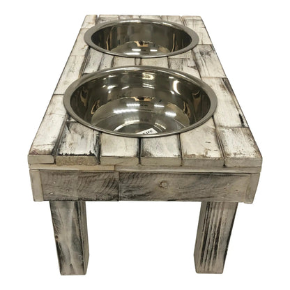 Close angled view of the white wash raised dog feeder from one end, looking down into the stainless bowls
