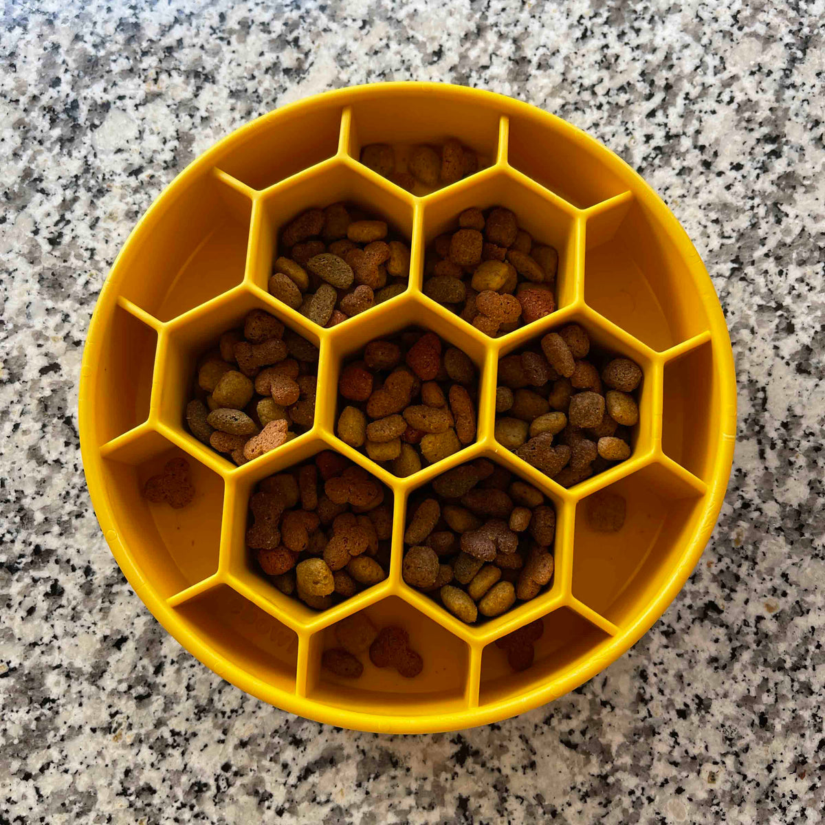 Yellow SodaPup Honeycomb eBowl from above with dry kibble in the center cells, on a granite counter