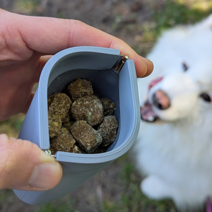 Up Dog One-Hand Treat Pouch squeezed open to show soft treats inside, white fluffy dog looking up for one
