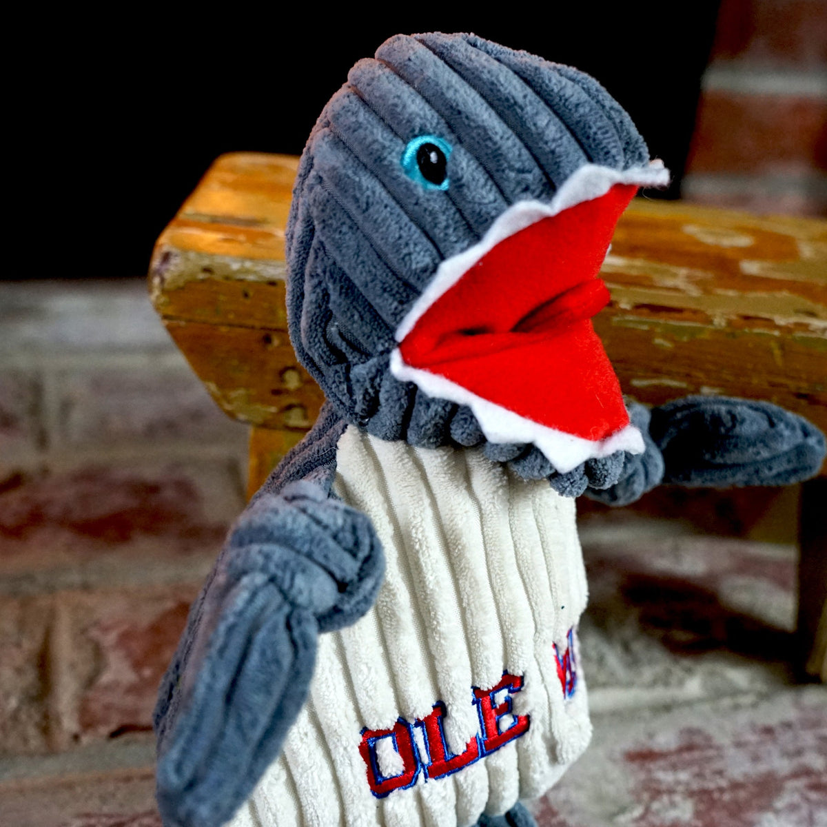 Landshark Knottie dog toy close-up on a brick hearth, blue eye and open red mouth edged in white felt teeth
