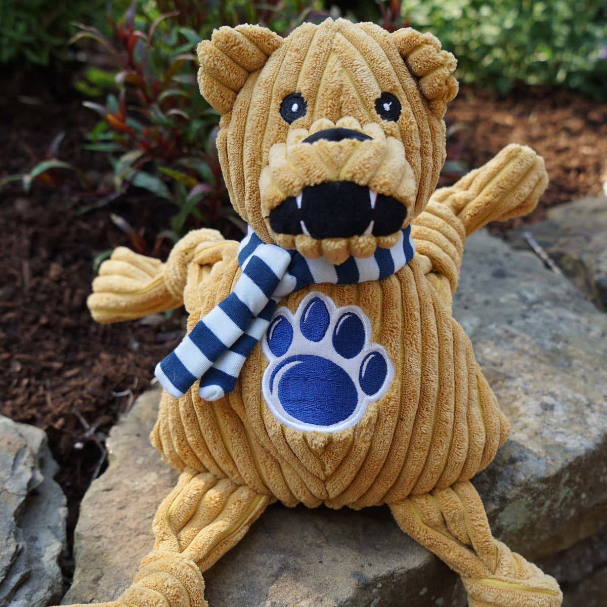 Nittany Lion Knottie dog toy sitting on a garden rock, open black mouth with white fangs and striped scarf
