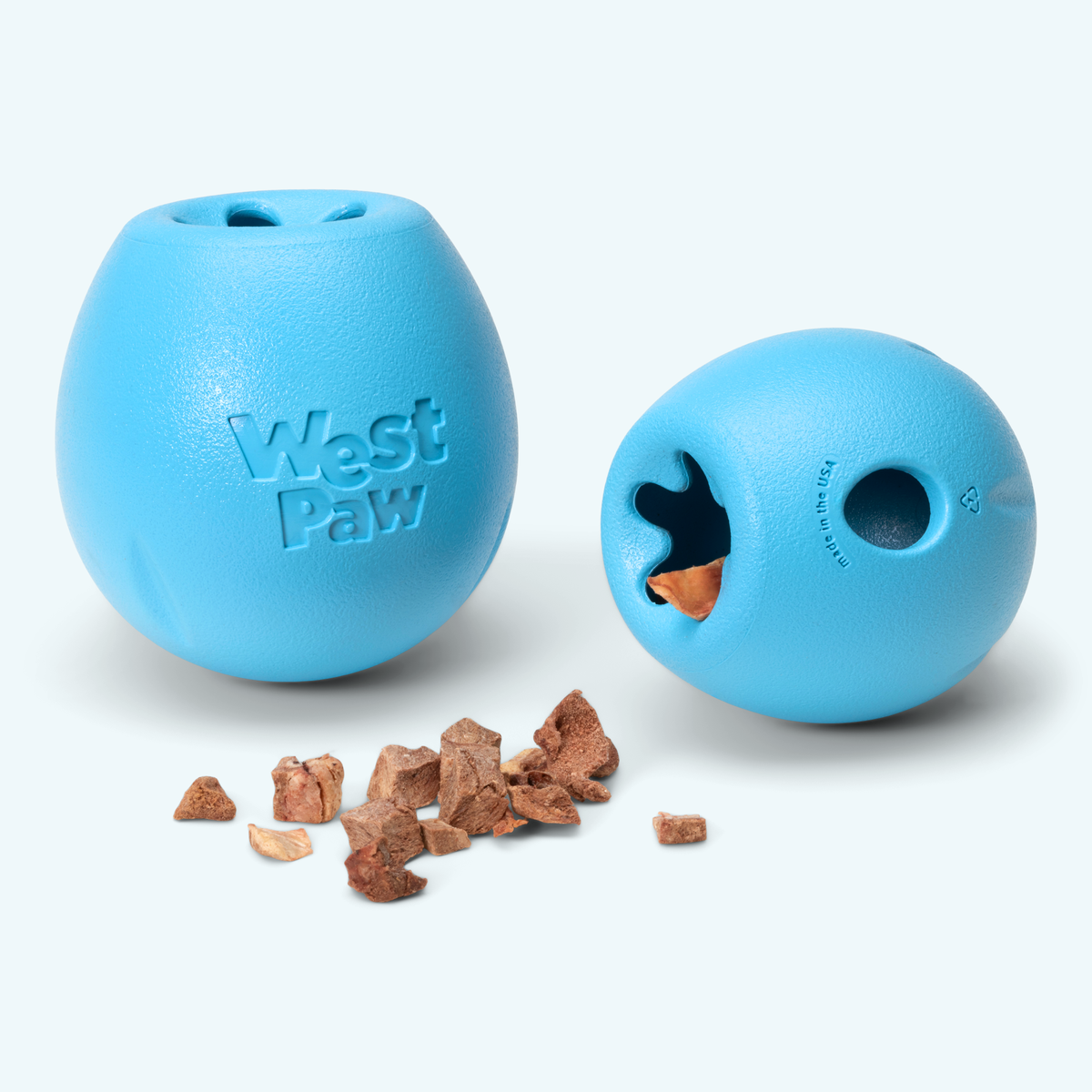 Rumbl treat dispensers in aqua, one tipped over to show the wavy opening and round side hole, treats spilled