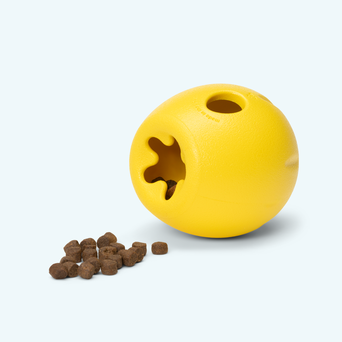 Rumbl treat dispenser in dandelion yellow tipped on its side beside a small pile of kibble