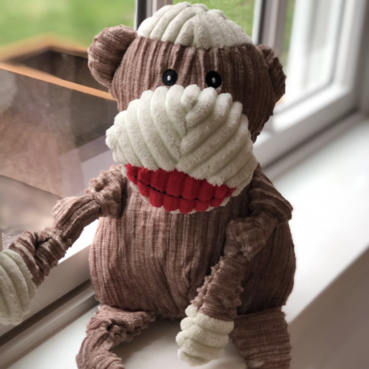 Stuey Sock Monkey Knottie sitting on a sunny windowsill, corduroy face and red lips toward the camera
