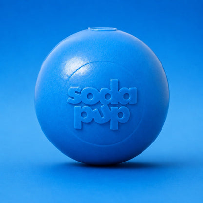 Light blue SodaPup Squeak Ball, front view on a blue background showing the embossed logo