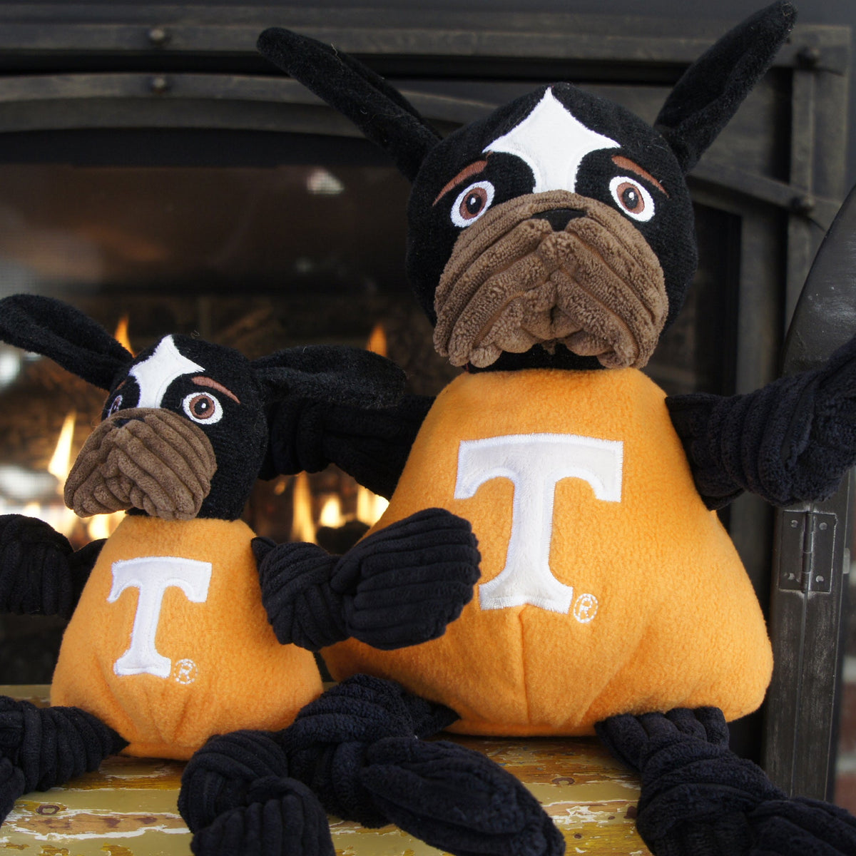 Smokey Knottie dog toy in two sizes sitting side by side in front of a fireplace