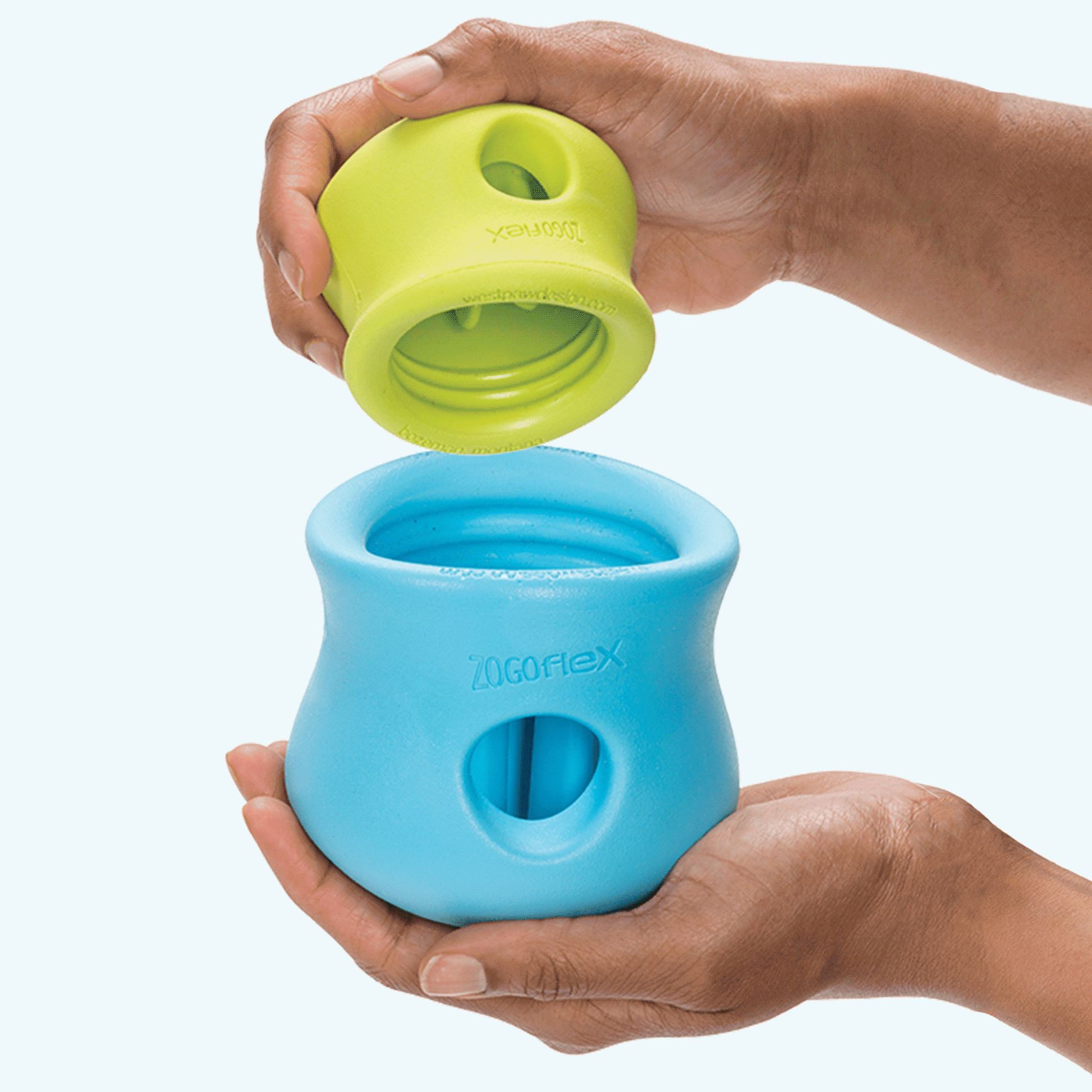 Hands fitting a small green West Paw Toppl into a larger aqua blue one and twisting it to lock