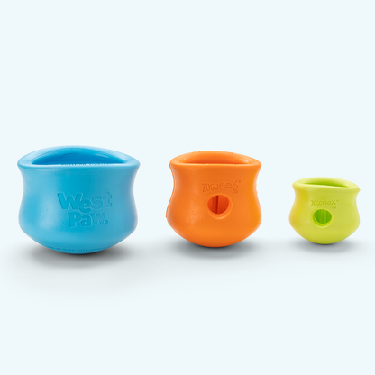 West Paw Toppl treat toys lined up by size: XL in aqua blue, Large in tangerine, and Small in green