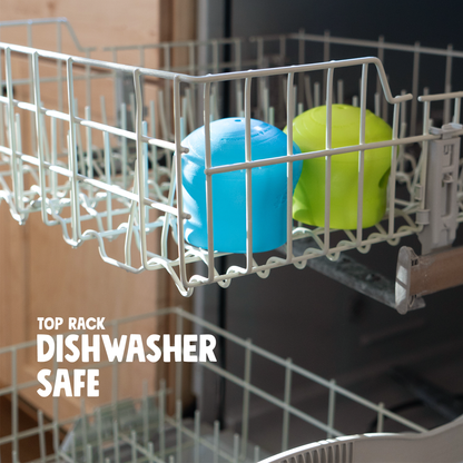 Aqua blue and green West Paw Toppl toys upside down on the top rack of a dishwasher, captioned dishwasher safe