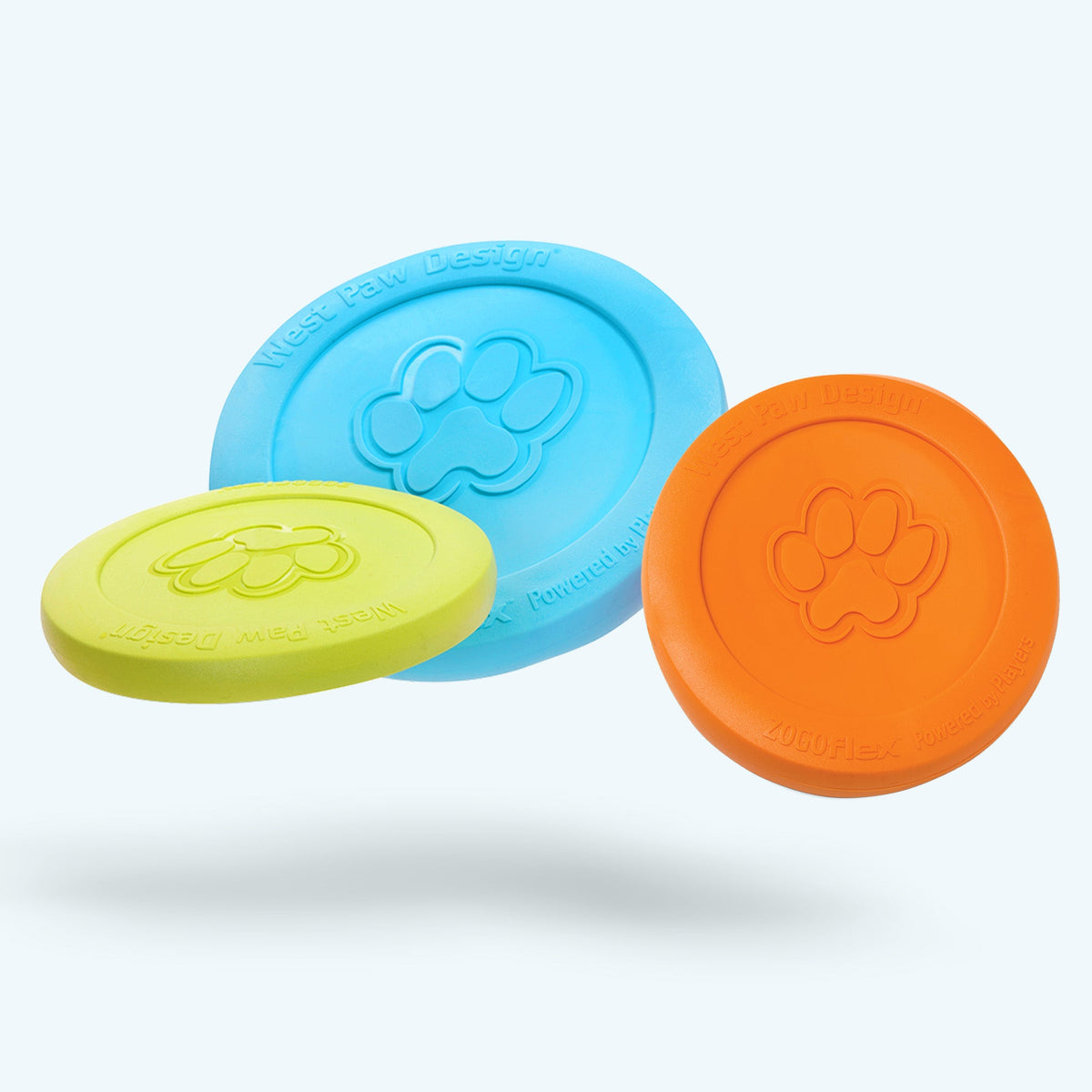 Three West Paw Zisc flying discs floating in the air in green, aqua blue, and tangerine