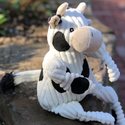 Dottie Cow Knottie dog toy sitting on a stone ledge outdoors, cream muzzle turned to the side