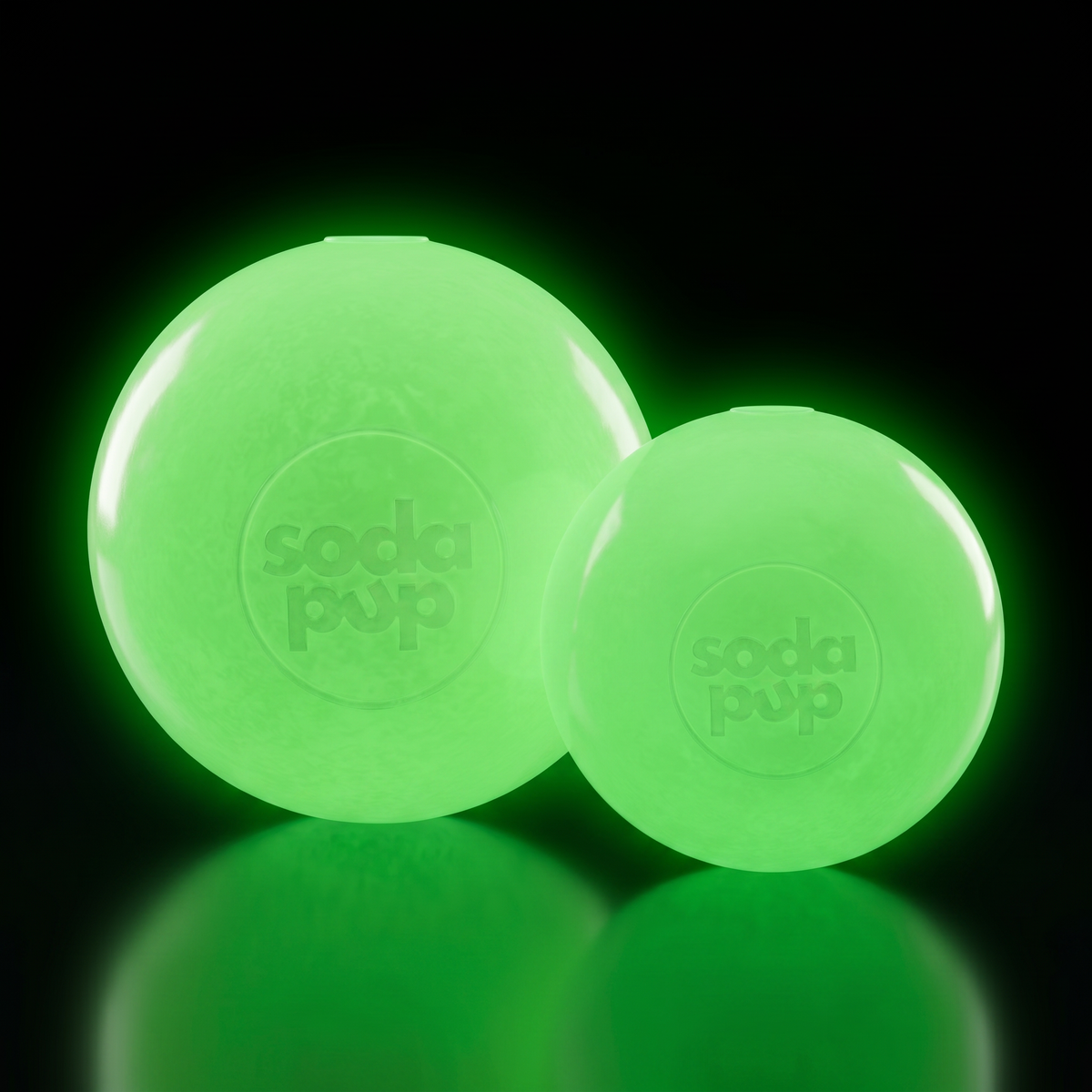 Large and Medium glow in the dark SodaPup Squeak Balls glowing green in the dark