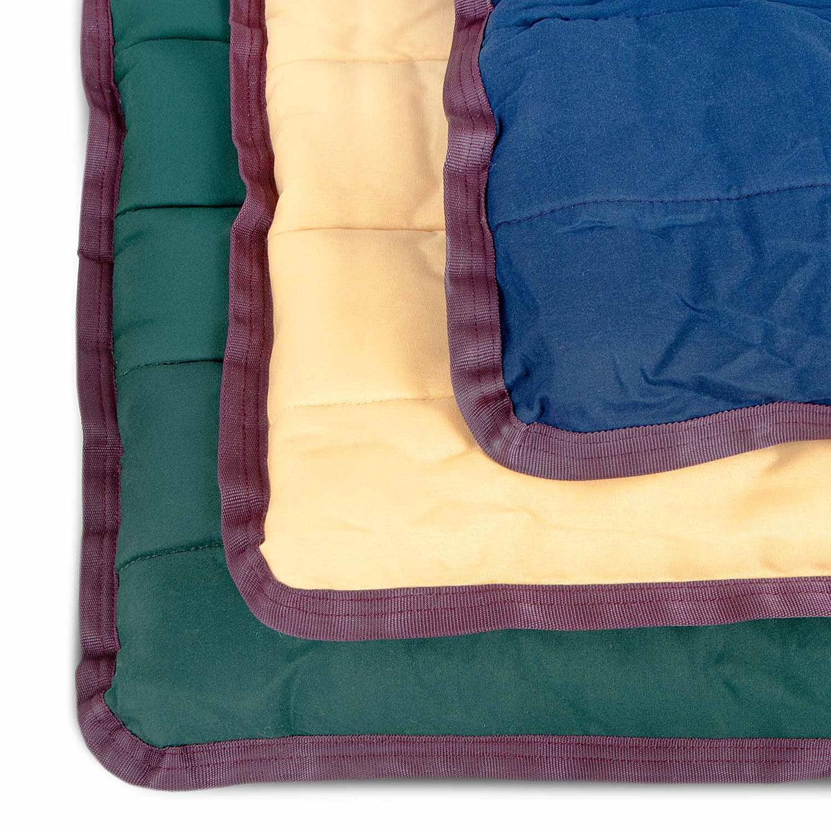 Corners of dark green, tan, and navy Jeffers crate pads stacked, showing the quilting and wine trim