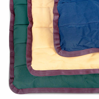 Corners of dark green, tan, and navy Jeffers crate pads stacked, showing the quilting and wine trim