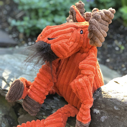 Morris Moose Knottie dog toy perched on a garden rock outdoors, side profile showing its shaggy beard and antlers